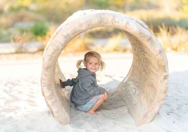 a girl in summer clothes is crouching in the sand on the beach