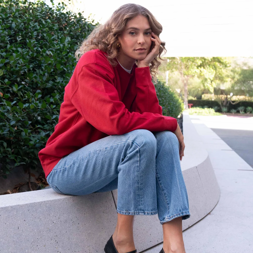 Woman wearing a red Cotton Heritage M2480 premium crewneck sweatshirt with light-wash jeans outdoors.